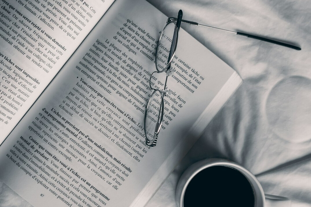 Open book with reading glasses and a cup of tea